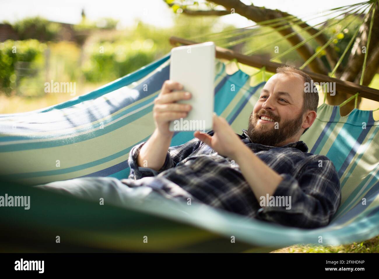 Happy man using digital tablet in sunny summer hammock Stock Photo