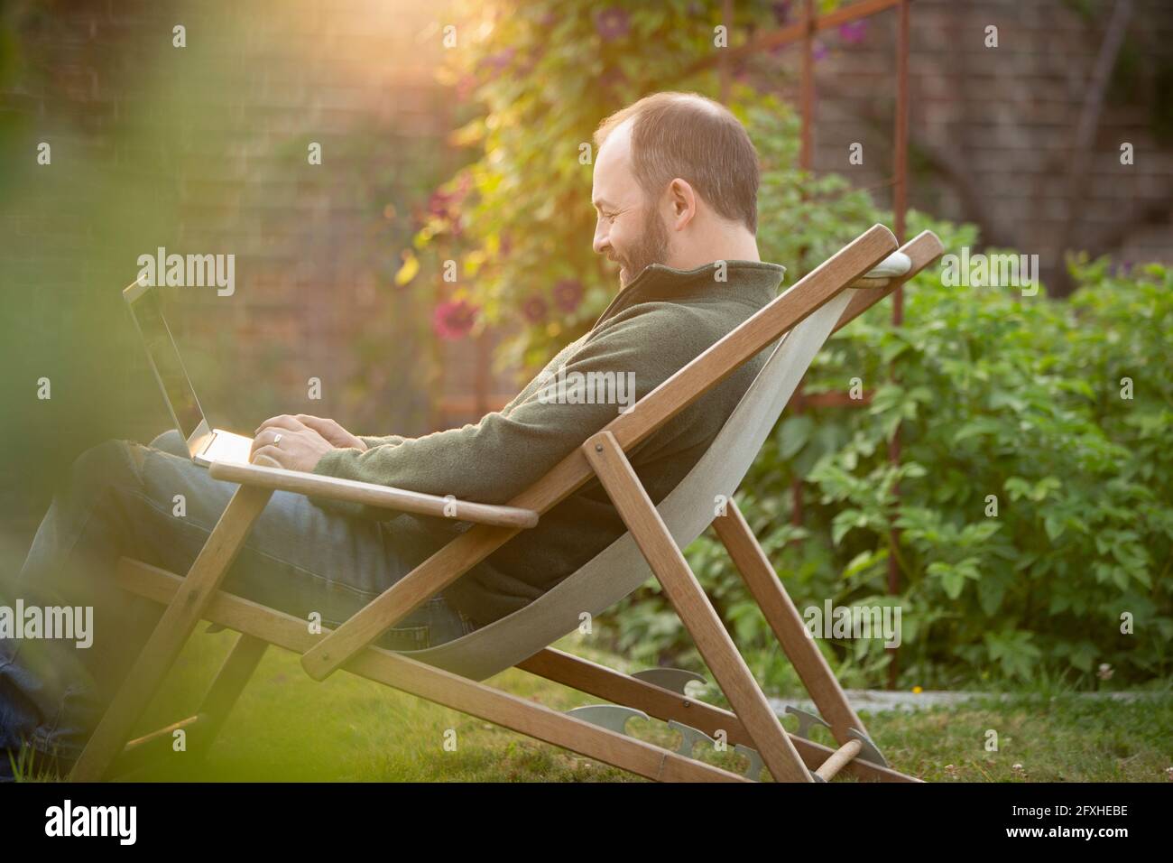 Man working at laptop in lawn chair in summer garden Stock Photo