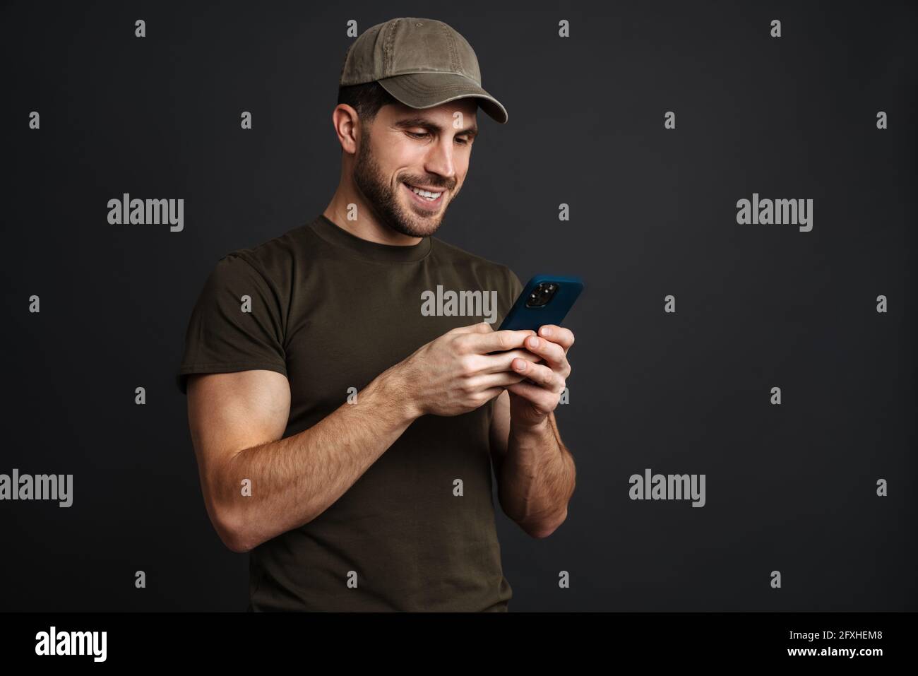 Happy masculine military man smiling and using mobile phone isolated over black background Stock Photo