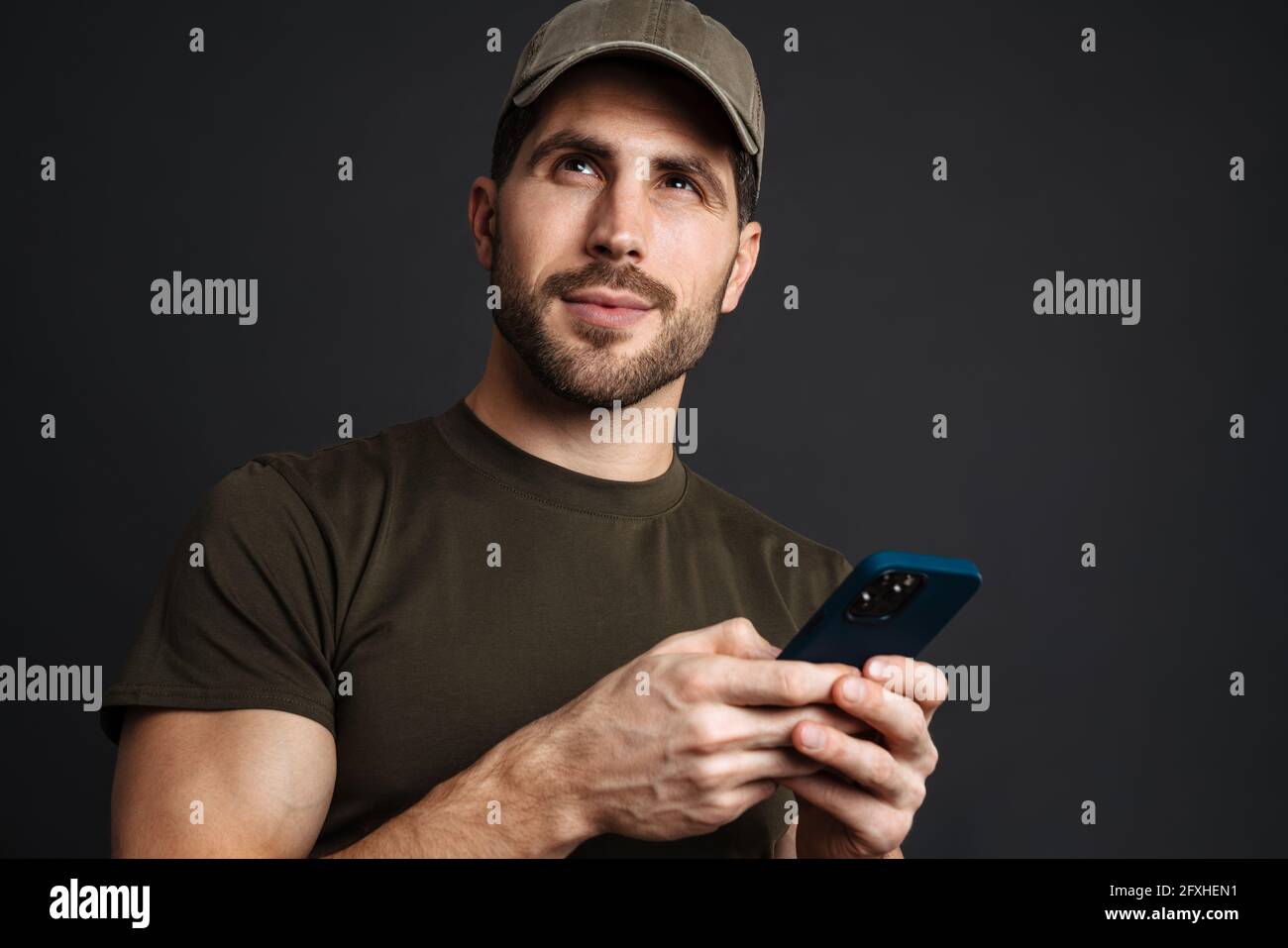 Pleased masculine military man using mobile phone isolated over black background Stock Photo