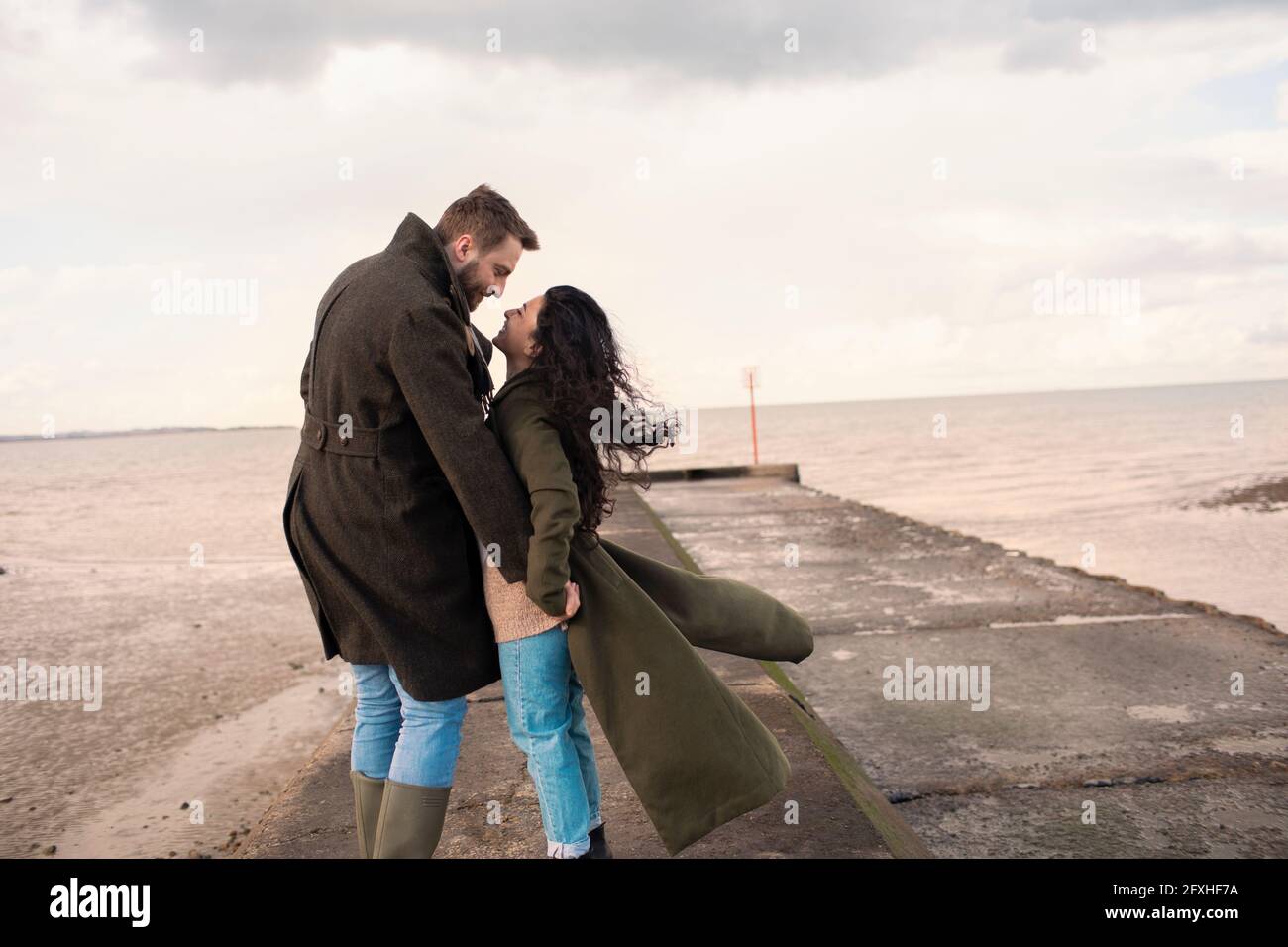 Happy affectionate couple in winter coats on ocean beach Stock Photo