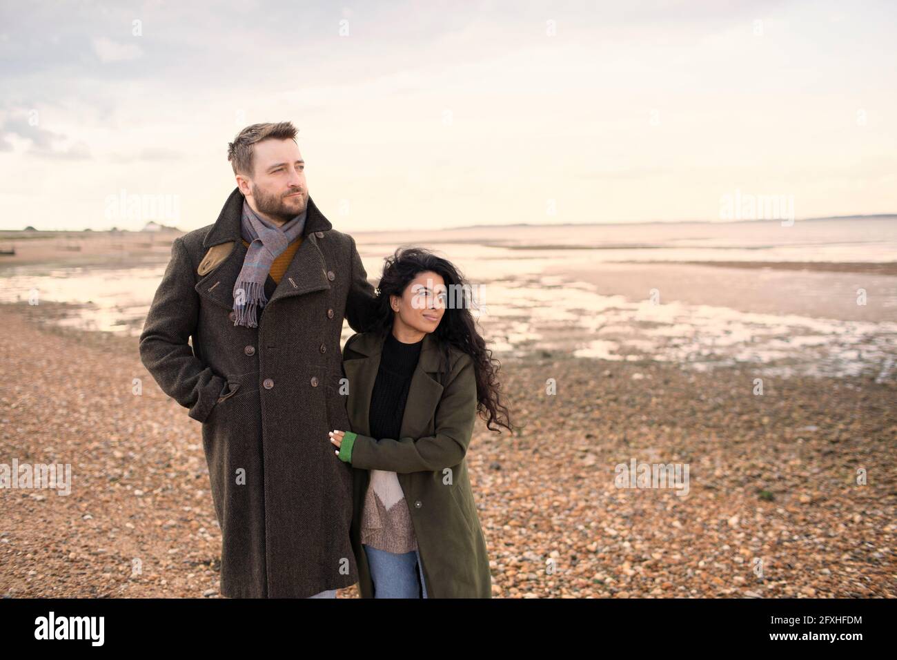 Affectionate couple in winter coats walking on ocean beach Stock Photo