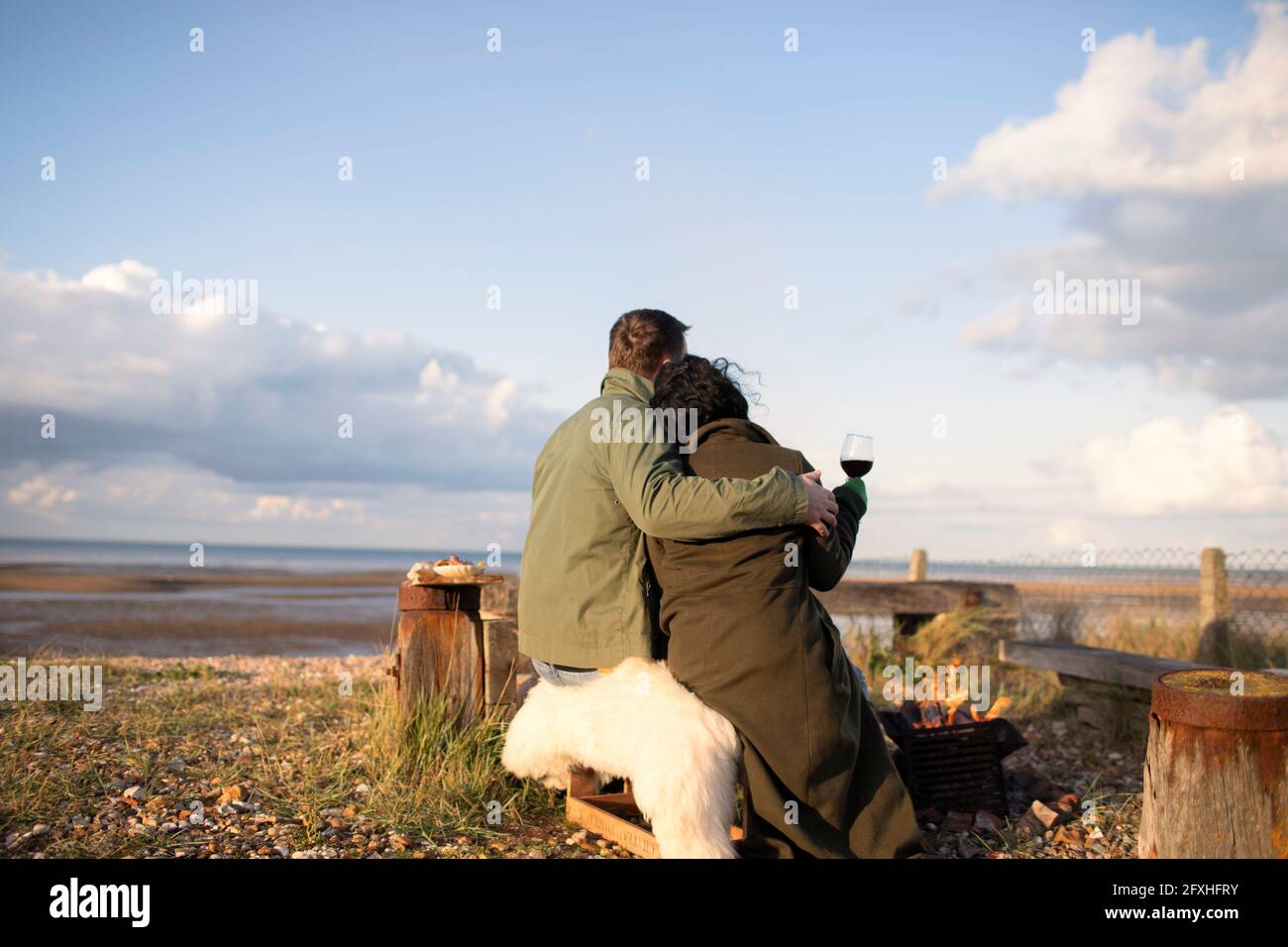 Affectionate couple hugging and drinking wine on sunny winter beach Stock Photo