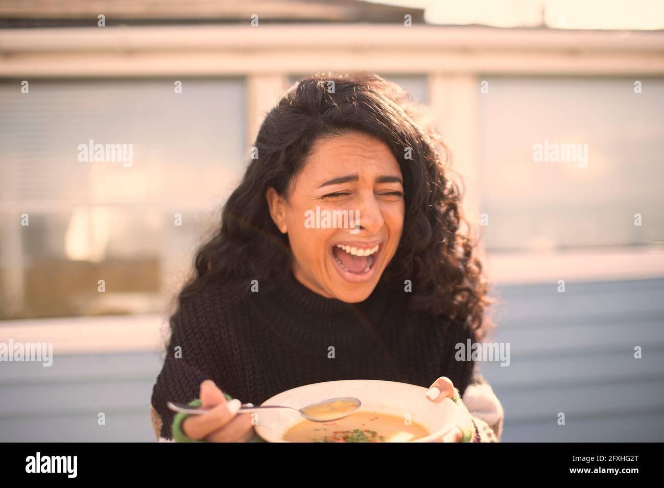 Happy laughing woman eating chowder on sunny patio Stock Photo