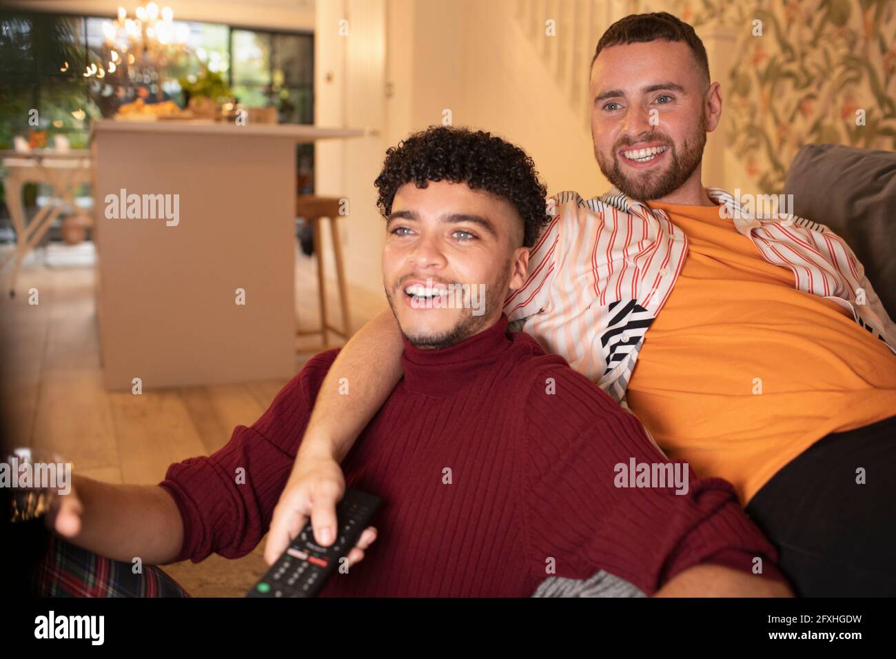 Happy gay male couple watching TV on sofa Stock Photo