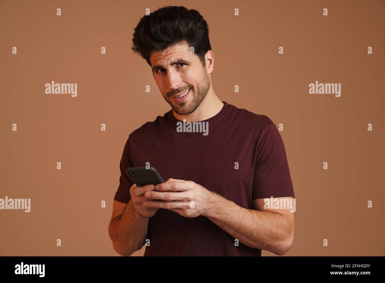 Pleased masculine man using mobile phone and smiling isolated over beige background Stock Photo