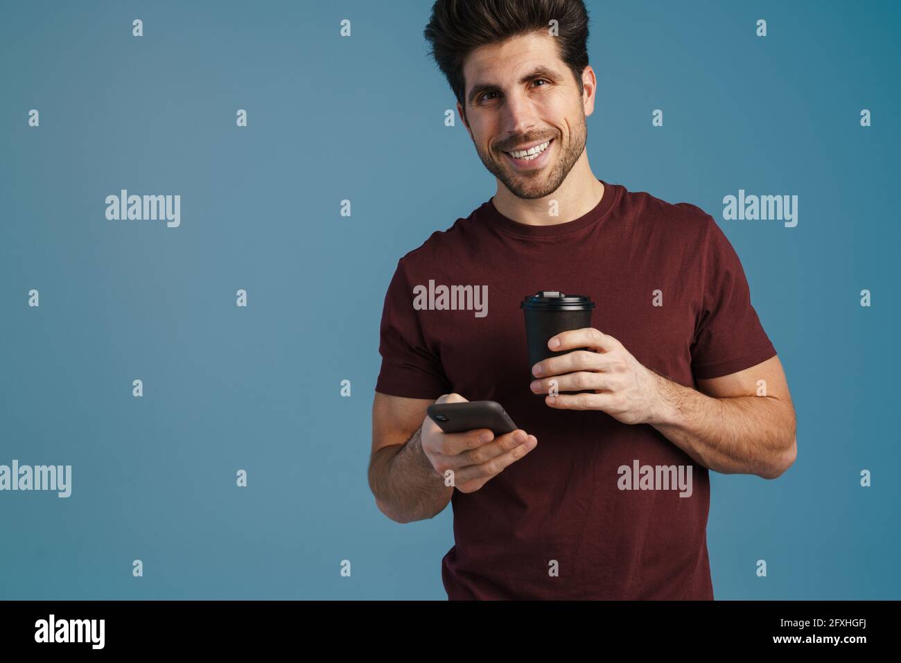 Happy handsome man drinking coffee and using mobile phone isolated over blue background Stock Photo