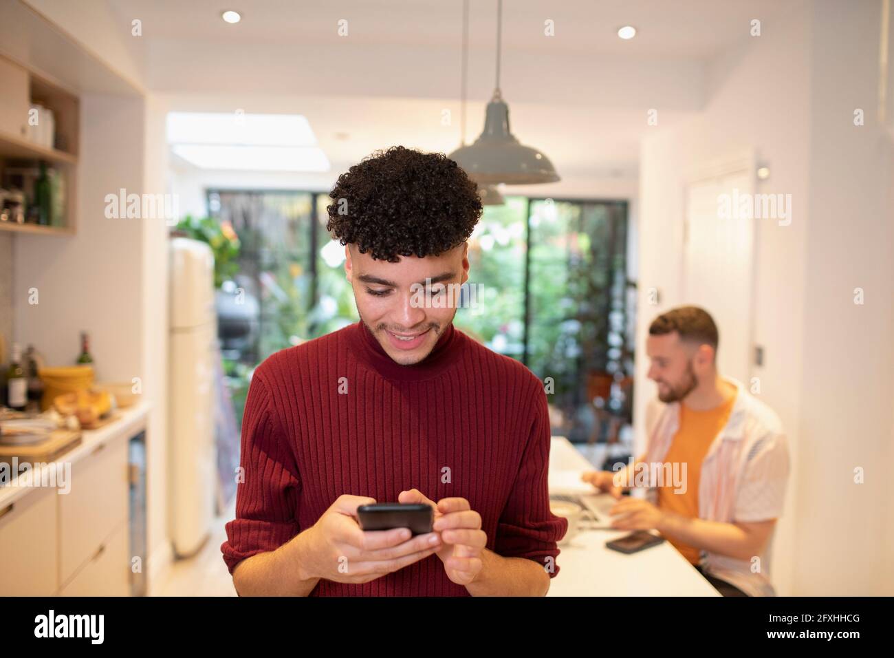 Young man using smart phone in kitchen Stock Photo