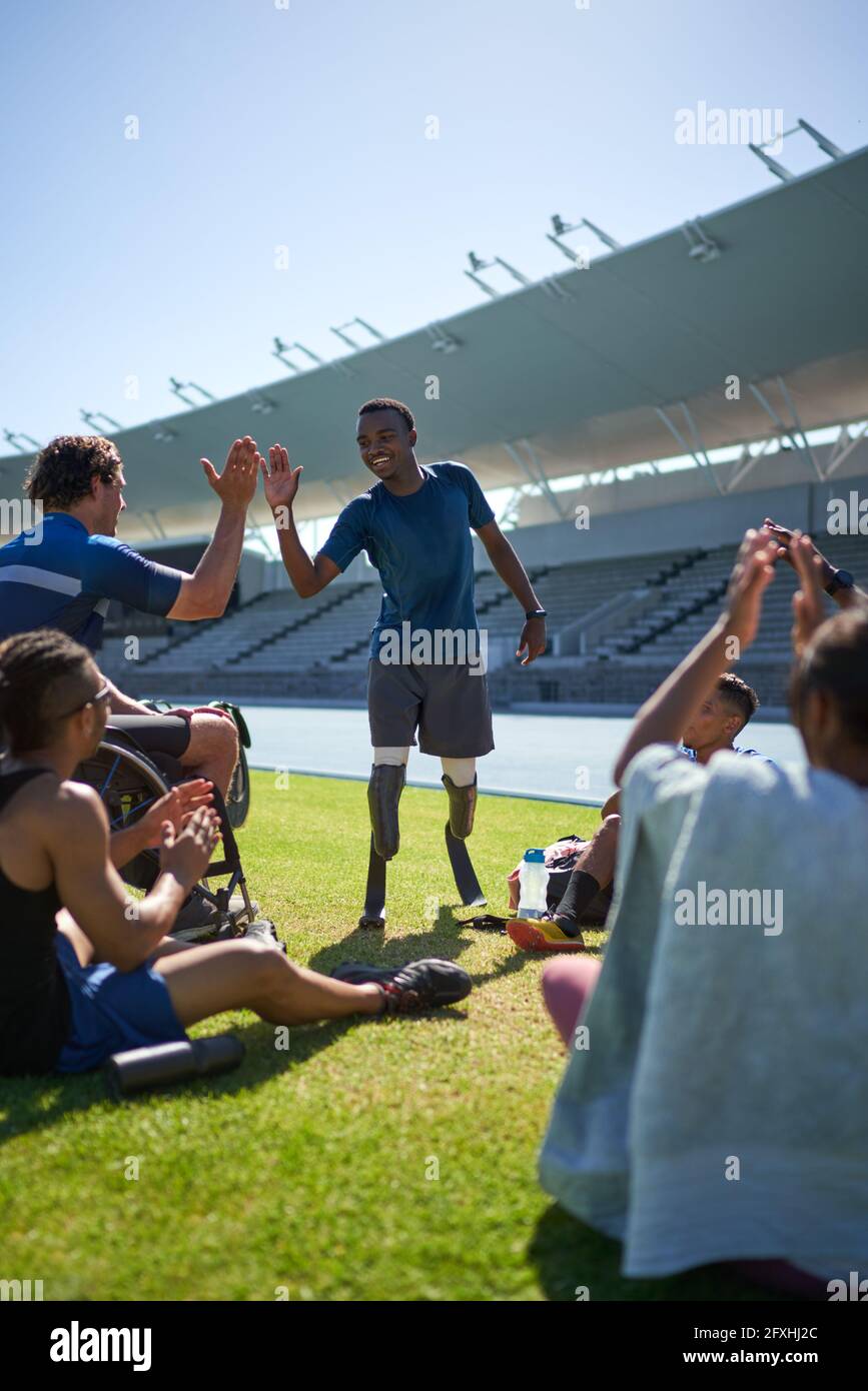 Male amputee and paraplegic athletes high fiving in sunny stadium Stock Photo