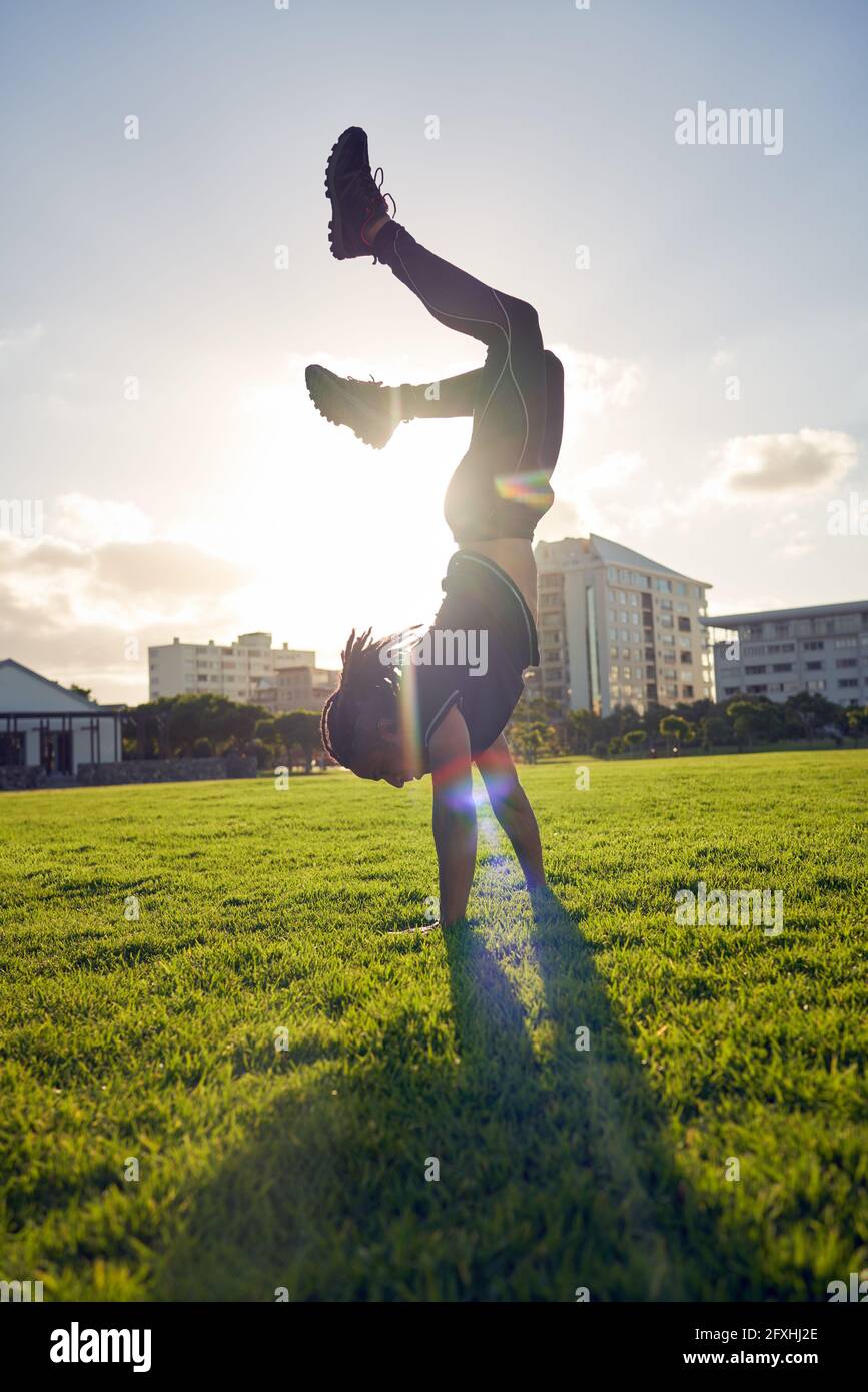 Carefree young man doing handstand in sunny park grass Stock Photo