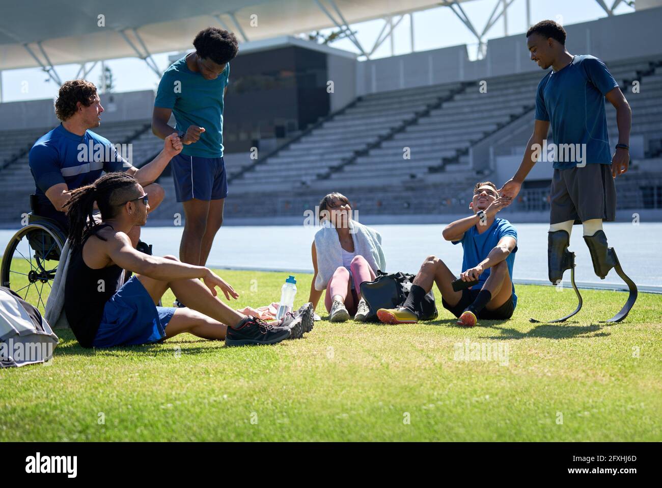 Amputee and paraplegic athletes fist bumping in sunny stadium Stock Photo