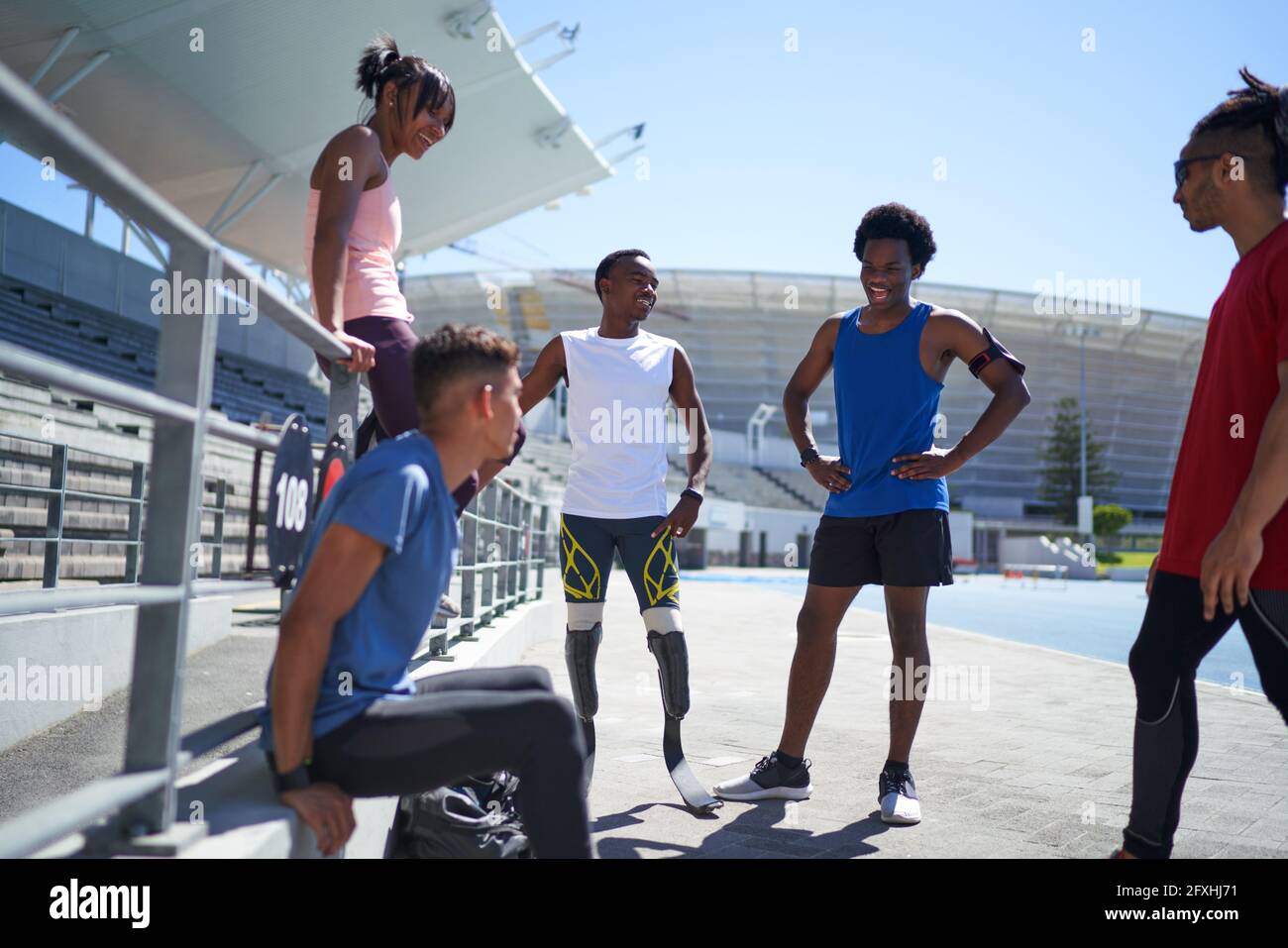 Runner and amputee friends talking on sunny sports track Stock Photo