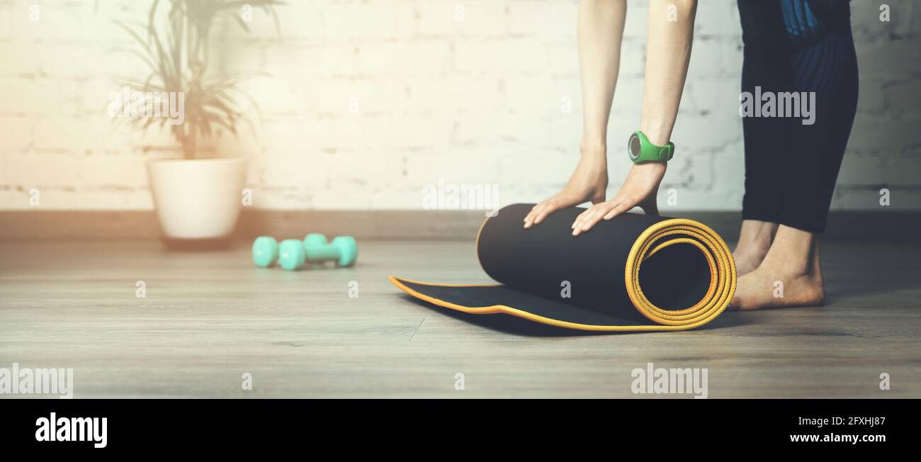 yoga practice or fitness workout at home. woman rolling exercise mat in room. banner copy space Stock Photo