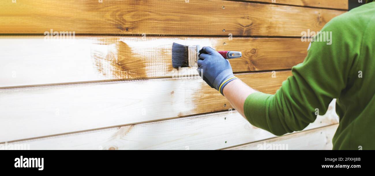 man painting wood house exterior siding with brown protective paint. banner copy space Stock Photo