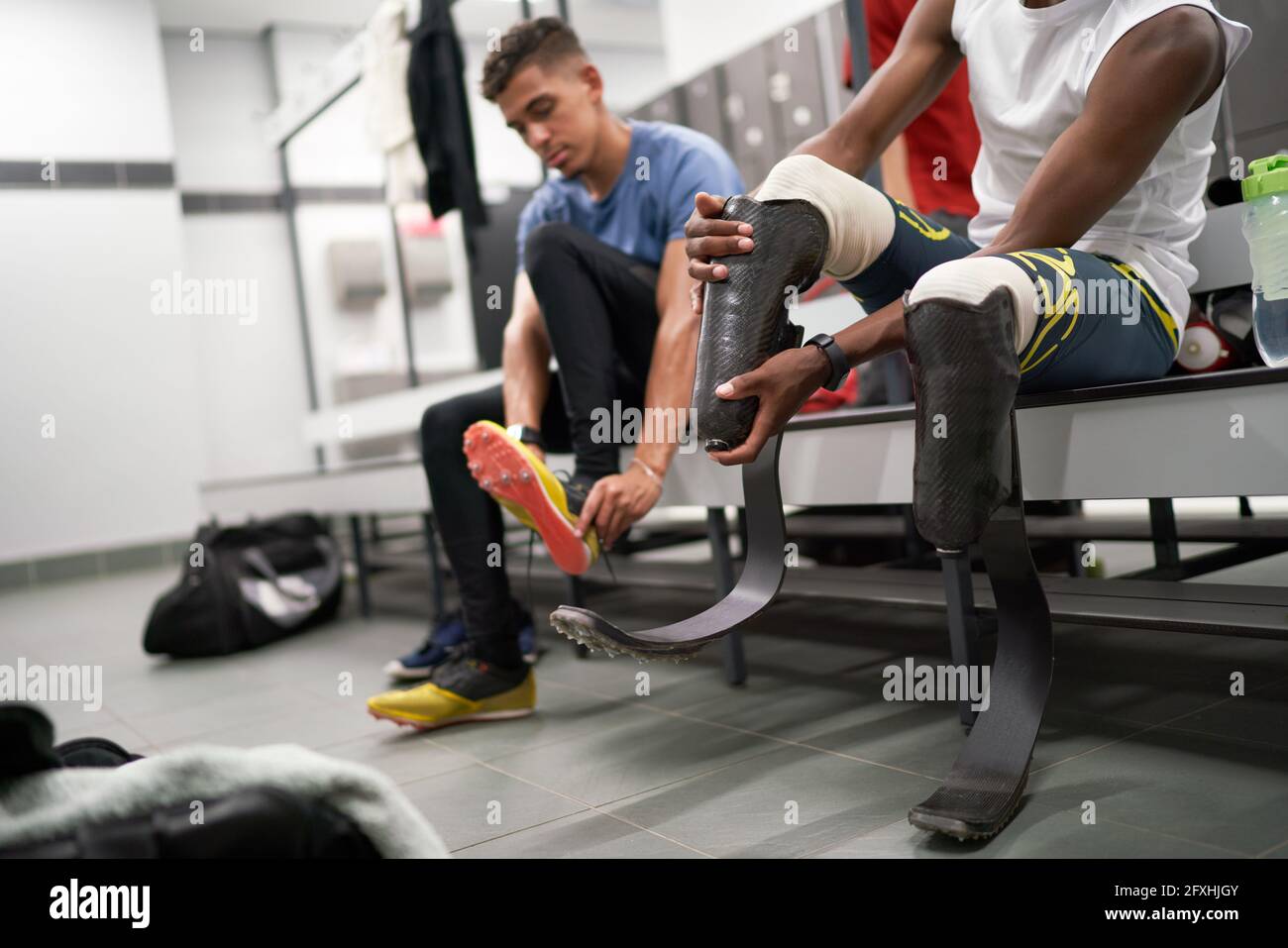 Male amputee athlete adjusting running blade prosthetic in locker room Stock Photo