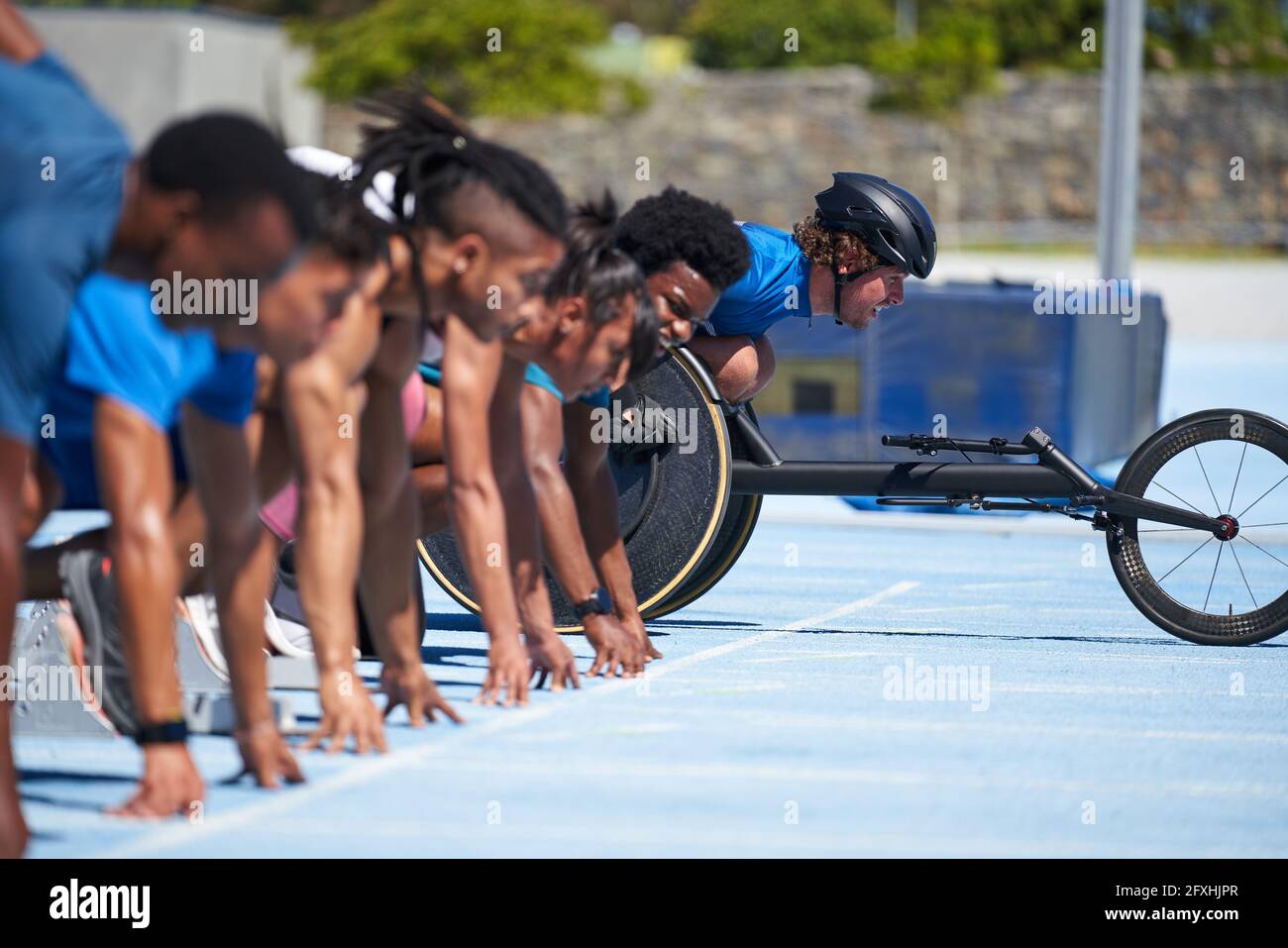 Wheelchair athlete at starting line with sprinters on sunny track Stock Photo