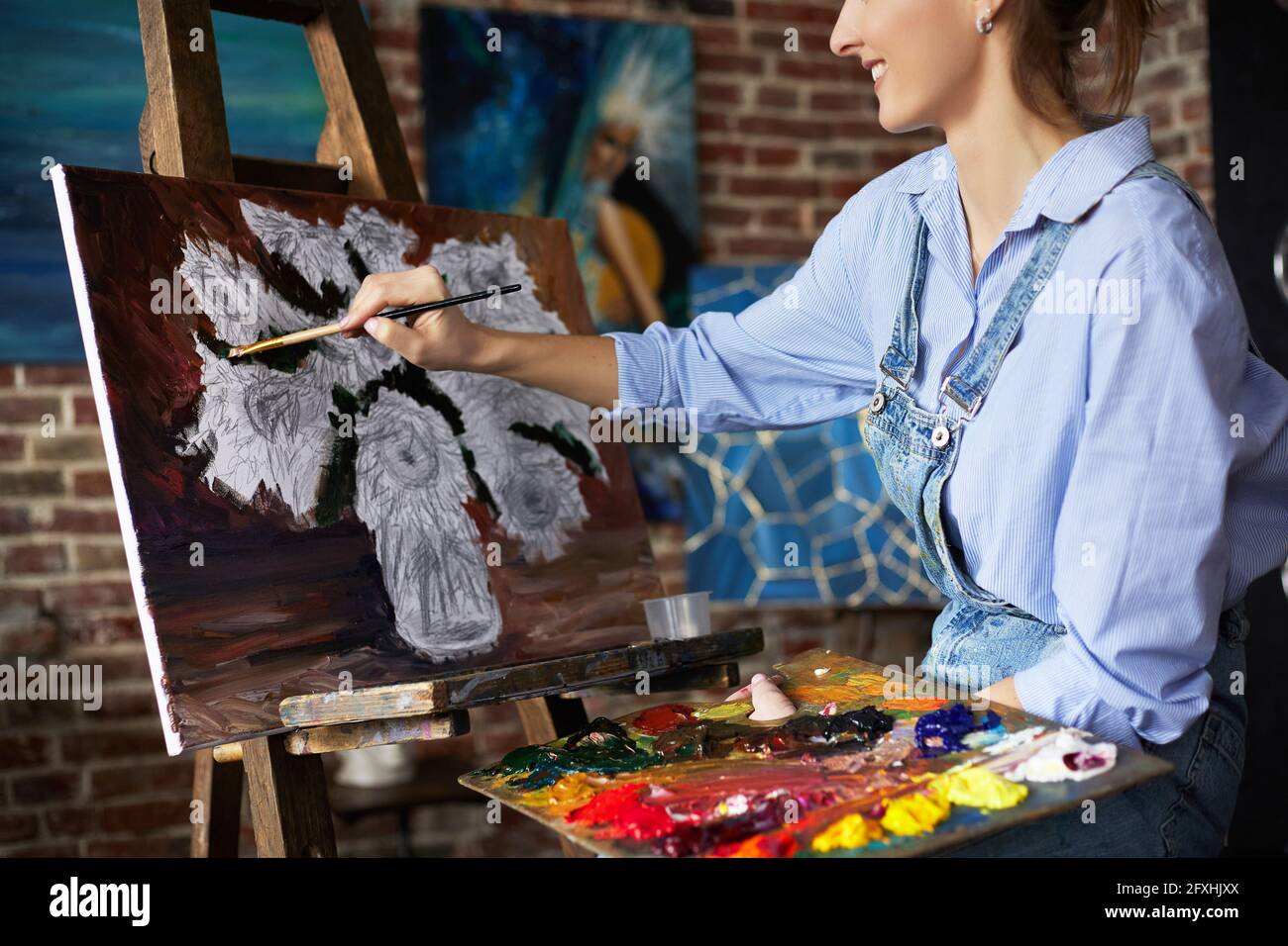Young beautiful female artist painting still life with sunflower on ...