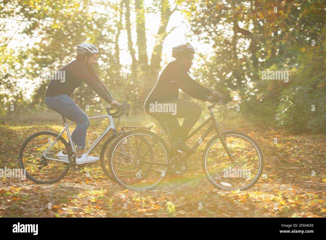 Couple bike riding through autumn leaves in sunny park Stock Photo