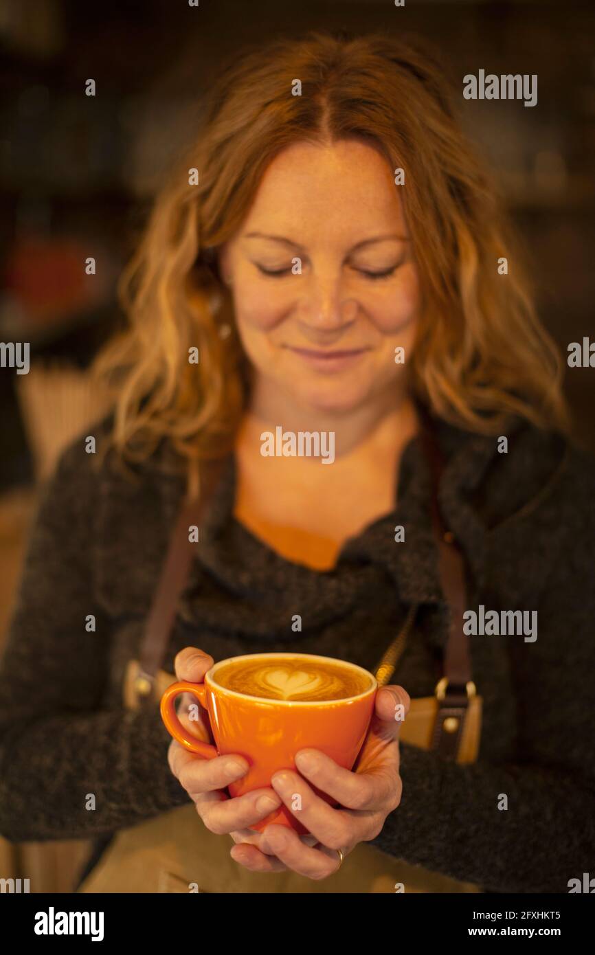 Happy female barista holding cappuccino with heart shape foam Stock Photo