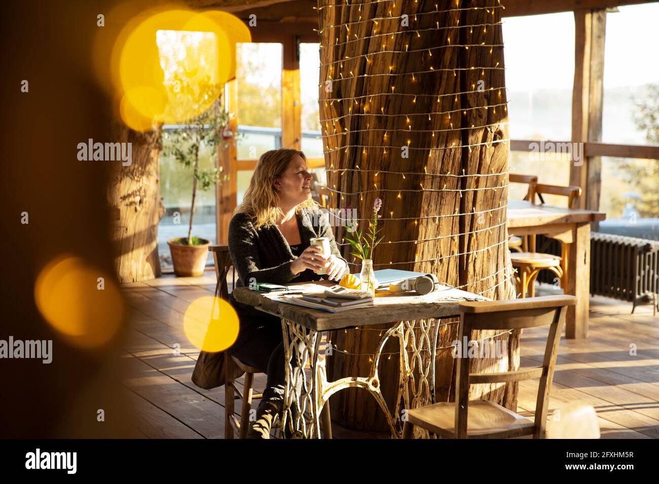 Female small business owner drinking coffee at sunny cafe table Stock Photo