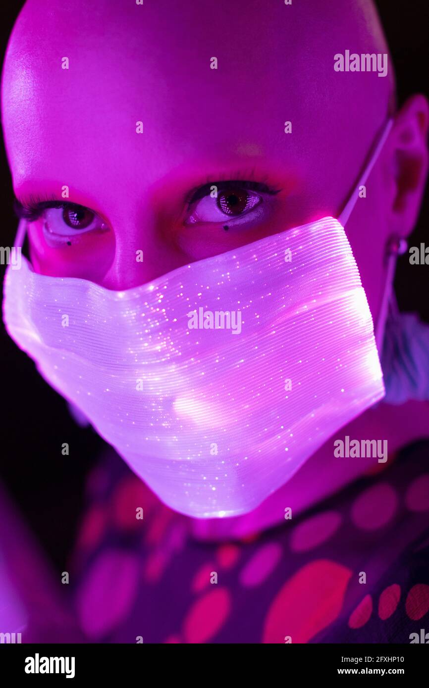 Close up portrait woman with shaved head in glowing face mask Stock