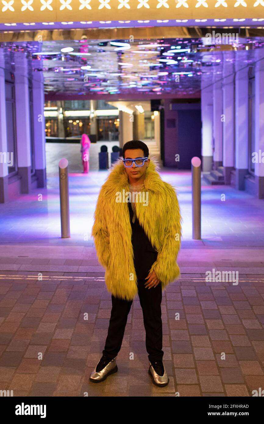 Portrait stylish young man in feather coat under neon city lights Stock Photo