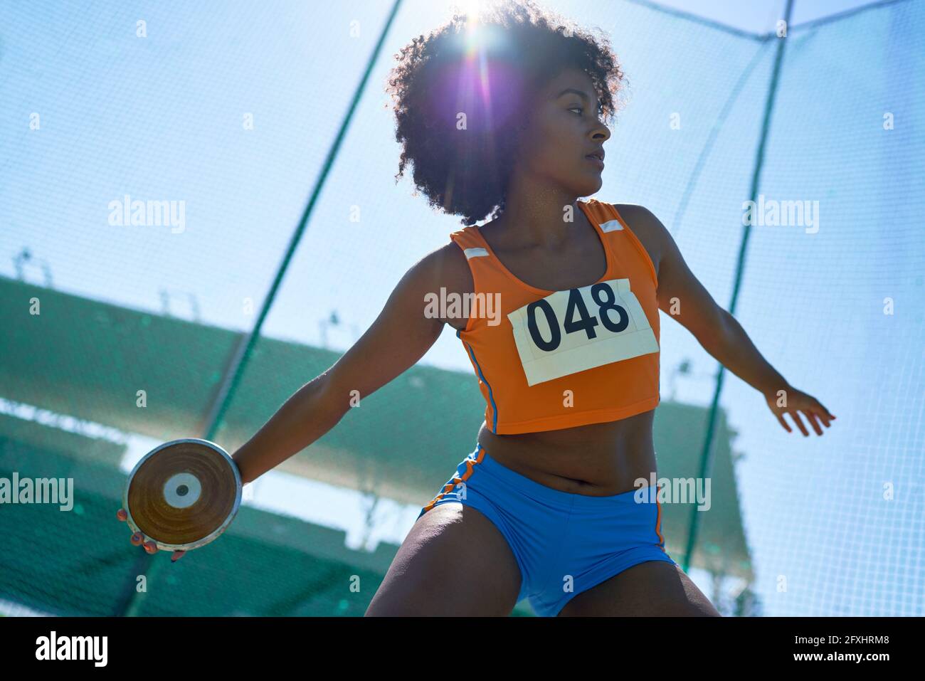 Female track and field athlete throwing discus under sunny blue sky Stock Photo