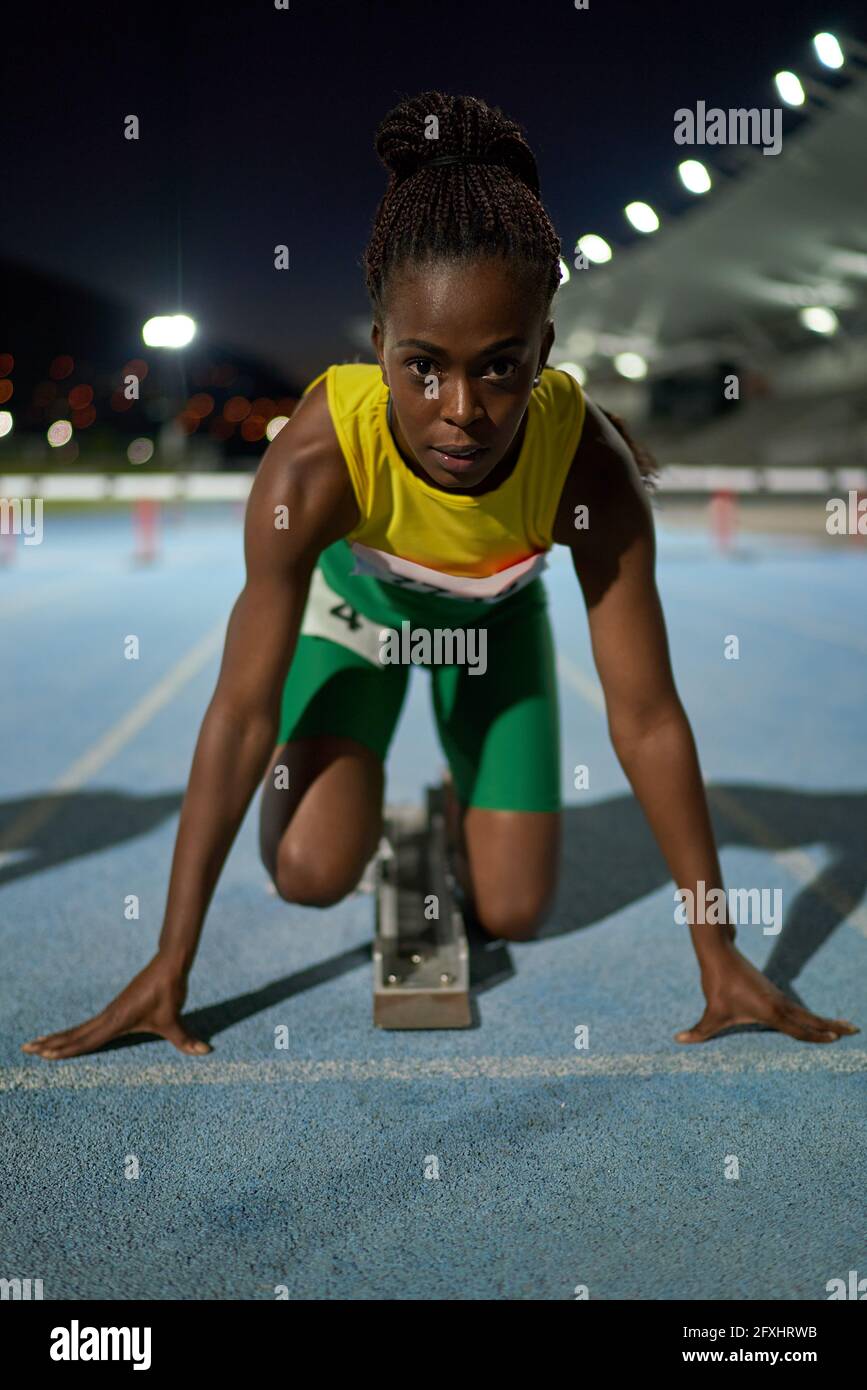 Portrait focused female track and field athlete at starting block Stock
