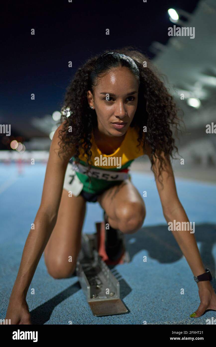 Determined female track and field athlete at starting block on track