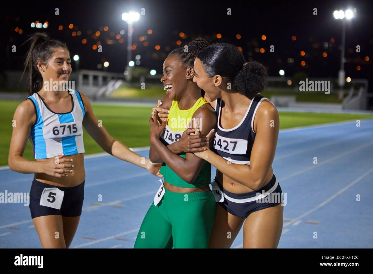 Happy female track and field athletes celebrating and hugging on track