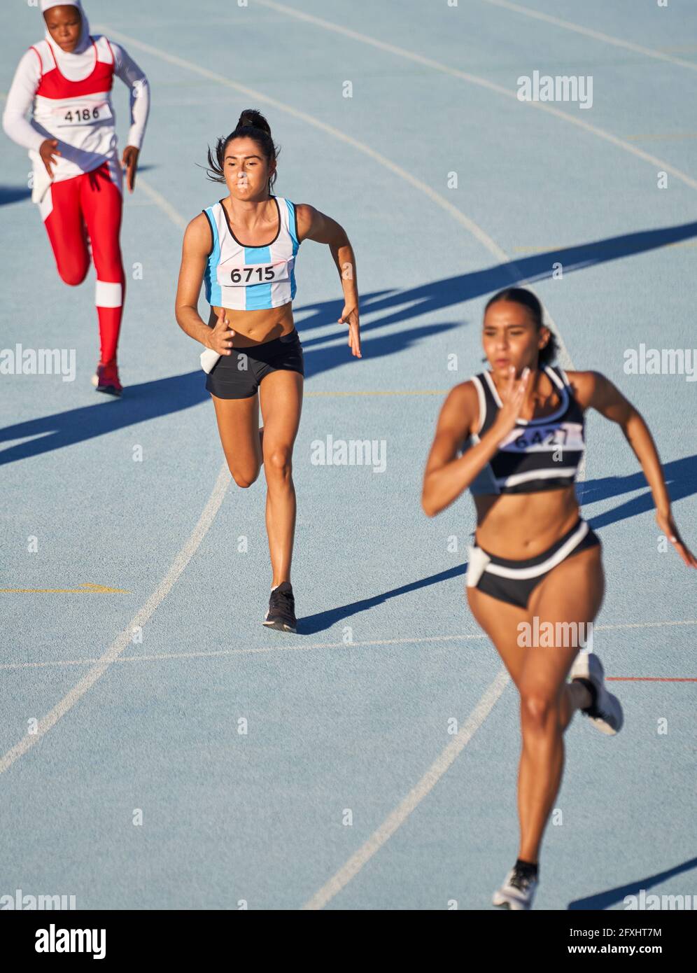 Female athletes running in competition on blue track - Stock Image