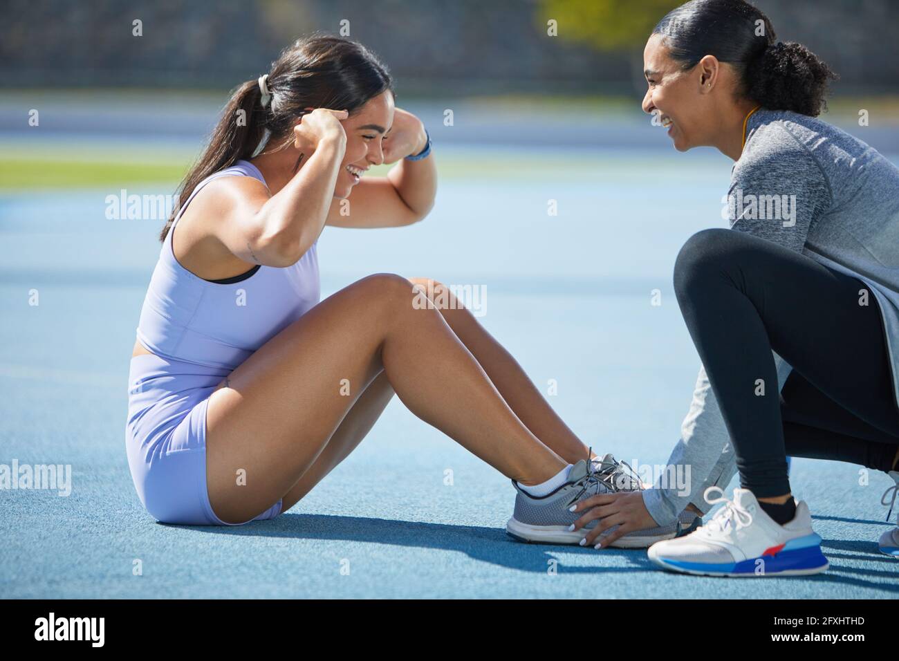 Happy female track and field athletes doing sit ups on track Stock Photo