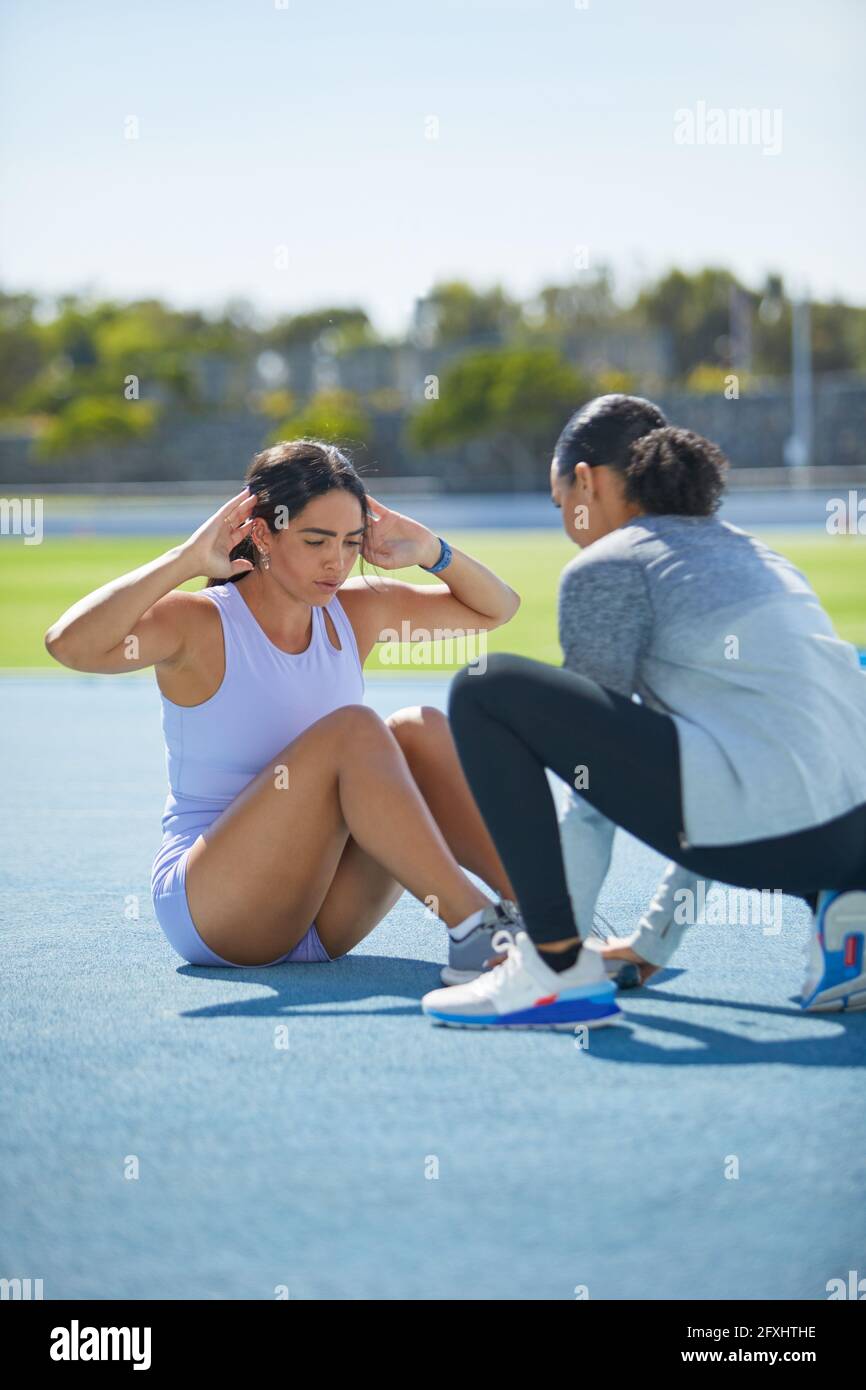 Female track and field athletes doing sit ups on sunny track Stock Photo
