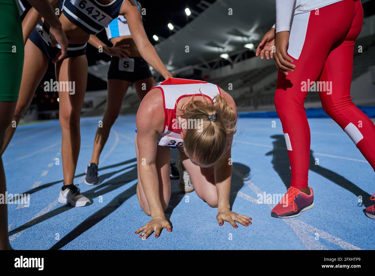 Female track and field athletes supporting tired runner on track Stock