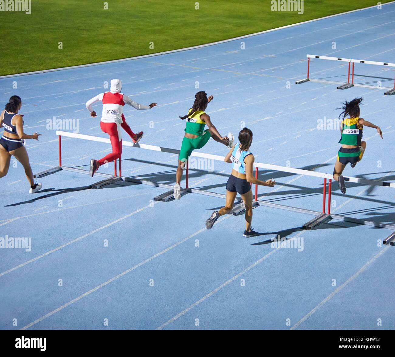 Female track and field athletes jumping hurdles in competition Stock