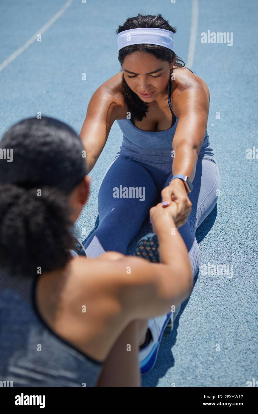 Female track and field athletes stretching on sunny track Stock Photo