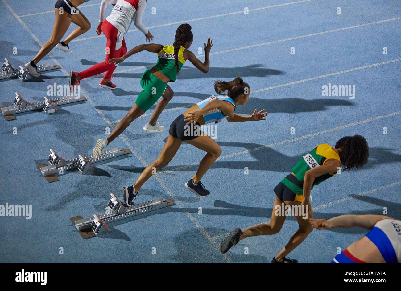 Female track and field athletes taking off from starting blocks Stock