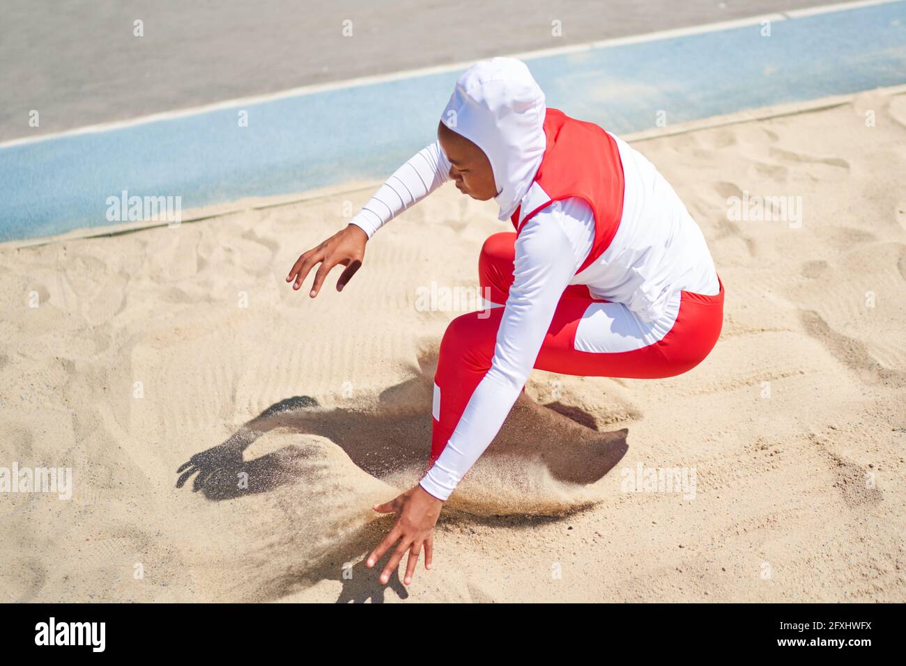 Female track and field athlete in hijab long jumping in sand Stock Photo
