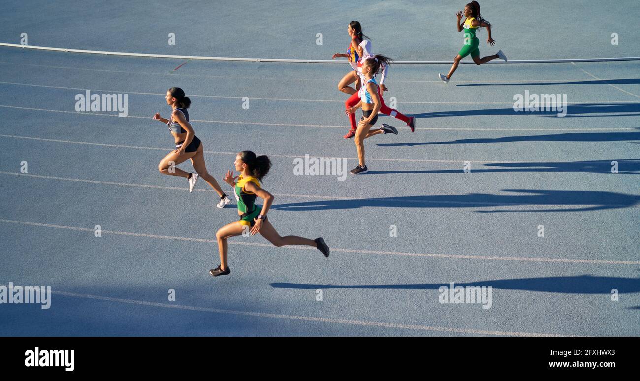 Female track and field athletes running in competition on blue track Stock Photo