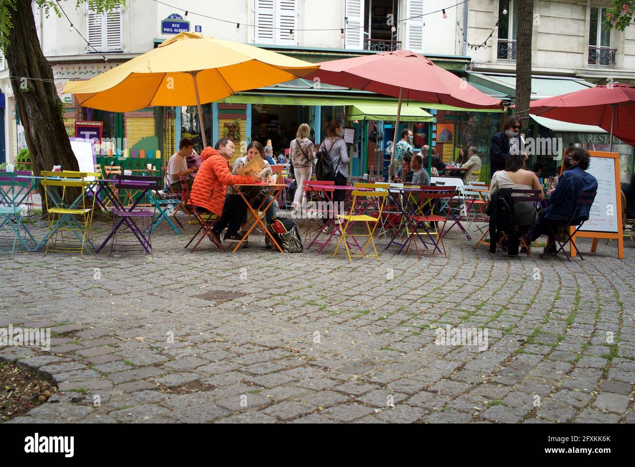 People enjoy a drink on a colourful café terrace, one of many terraces now open to the public after Covid-19 lockdown restrictions are eased - L'Été en Pente Douce, 8 Rue Paul Albert, 75018, Paris, France. May 2021. Stock Photo