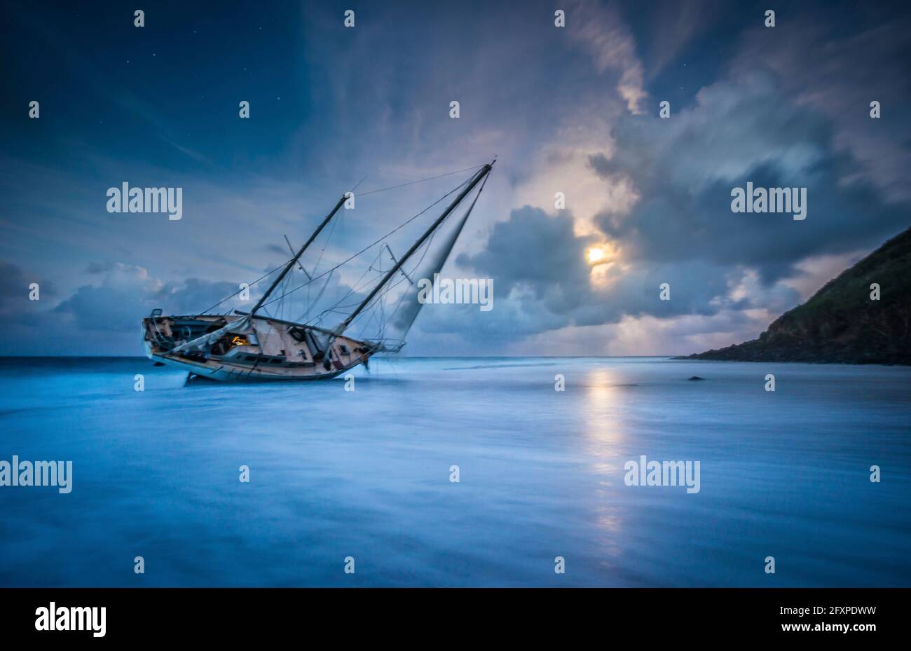 An abandoned sailboat rests on its side at low tide in Moloa'a Bay, and the full moon rises over the sea, Kiluea, Hawaii, USA, Pacific Stock Photo