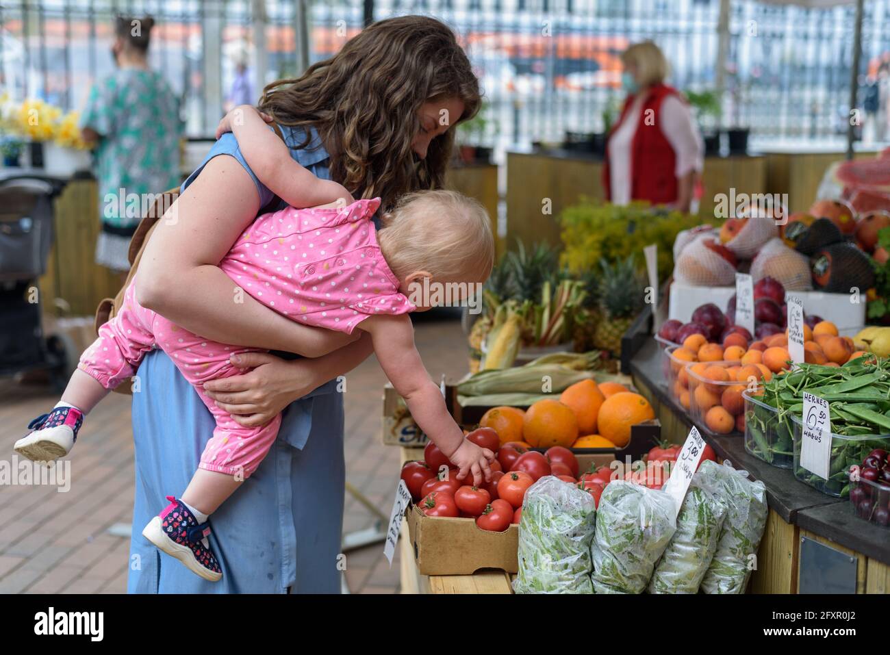 Woman buying vegetables with baby girl on farmers food market Stock