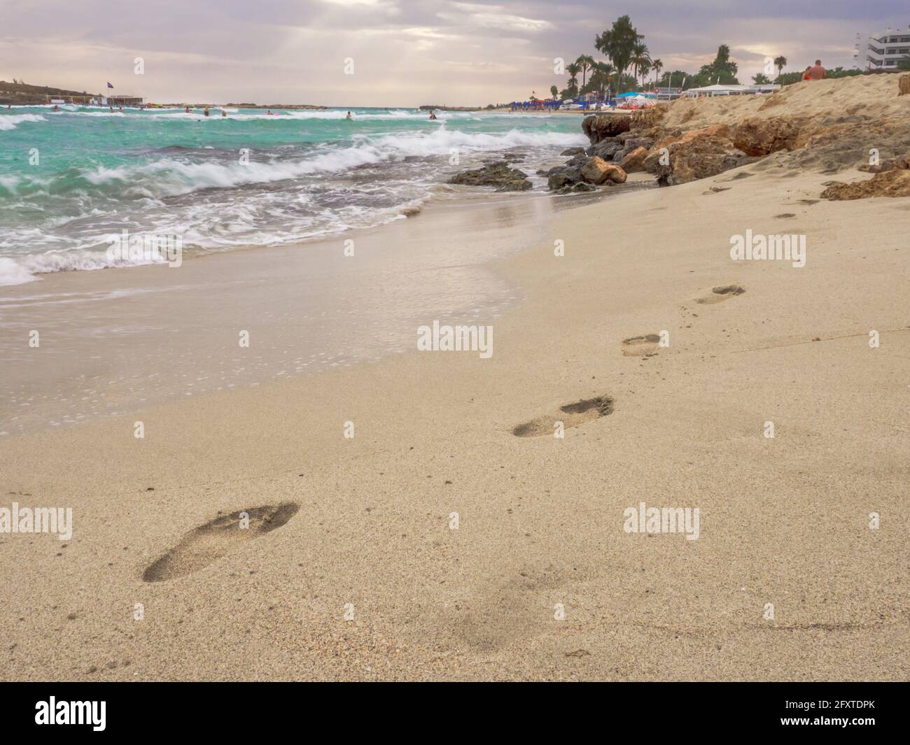 Empty picturesque Nissi beach with troubled cyan water, small rocky island, and dark cloudy sky in Ayia Napa, Cyprus. Delightful sea holidays. Stock Photo