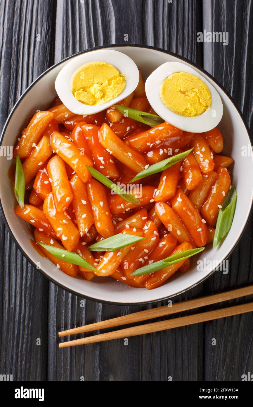 Korean tteokbokki spicy rice cake with eggs close-up in a bowl on the table. Vertical top view from above Stock Photo