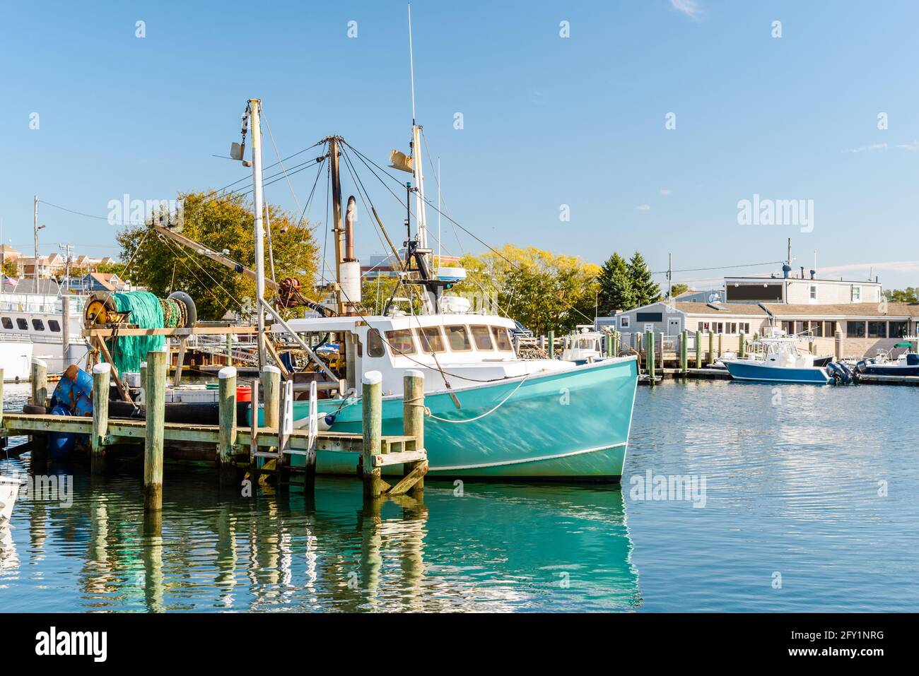 Fishing boat moored to a wooden pier in a harbour on a sunny autumn day. Reflection in water. Stock Photo
