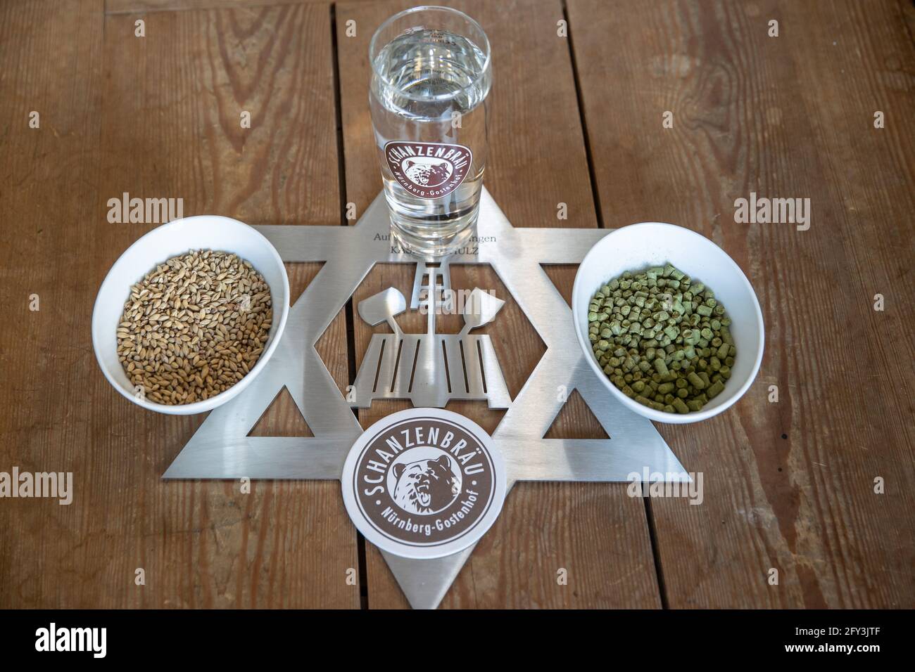 Nuremberg, Germany. 19th May, 2021. Barley malt (l), hop pellets and a glass of water stand on a brewer's star at the Schanzenbräu brewery in Nuremberg. The brewer's star, also known as the Zoiglstern, is made up of two interwoven triangles, and is used as the guild sign of the brewers and maltsters. Credit: Daniel Karmann/dpa/Alamy Live News Stock Photo