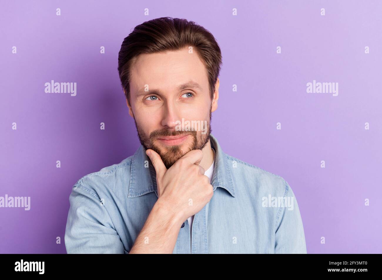 Photo of funny clever young guy wear denim clothes arm chim smiling looking empty space isolated purple color background Stock Photo