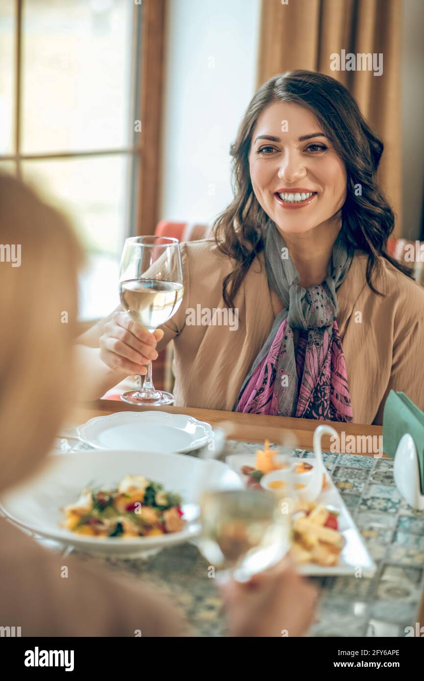 Smiling young woman holding a glass of wine and toasting with friends ...