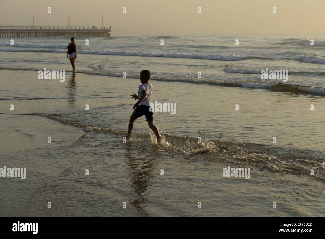 Boy on beach vacation running in water, play, seaside holiday, beautiful landscape, Durban waterfront, South Africa, child, joy, motion blur, happy Stock Photo
