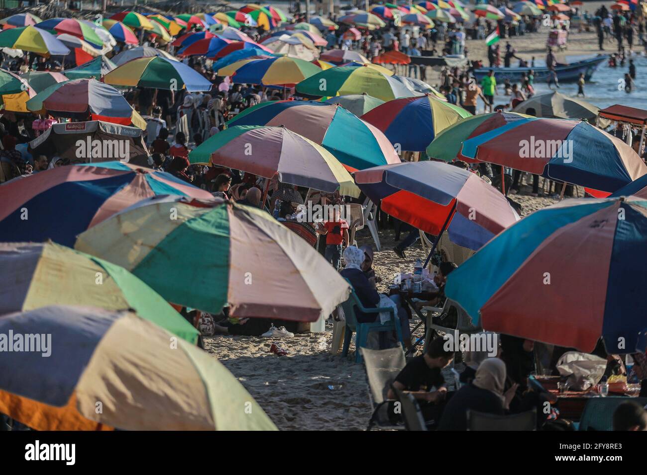 Gaza City, Palestinian Territories. 27th May, 2021. Palestinians sit under umbrellas along the shores of the Mediterranean, as life begins to return to normalcy, after a ceasefire was reached last week after 11 days of deadly confrontations between Israel and the Palestinian Islamist movement Hamas. Credit: Mohammed Talatene/dpa/Alamy Live News Stock Photo